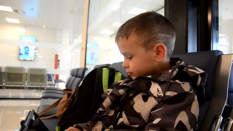 A boy sits at a train station or aroport while waiting for a train or plane Stock Footage 143611537