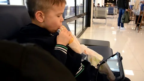 A boy sits at a train station or aroport while waiting for a train or plane 库存影片 143611724