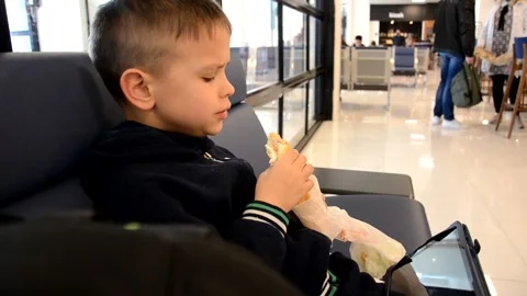 A boy sits at a train station or aroport while waiting for a train or plane 動画素材 143611735