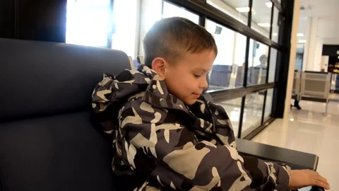 A boy sits at a train station or aroport while waiting for a train or plane Stock Footage 143611778
