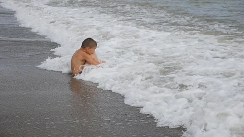 Boy sits in wave. wave with the head covers the child. slow motion Stock Footage 99463396
