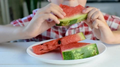 A boy sits at a white table in the kitchen and eats a watermelon with pleasure. Stock Footage 138687984