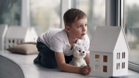 The boy sits on the windowsill and plays with a toy dog Stock Footage 141897439