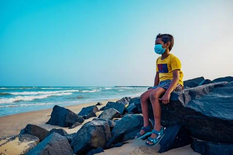 Boy sitting alone on the beach with medical mask - sad Indian Boy -Asian boy Stock Photos
