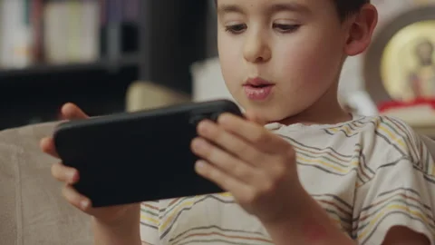 Boy sitting in an armchair in a room using phone, playing a video game or Stock Footage 243147125