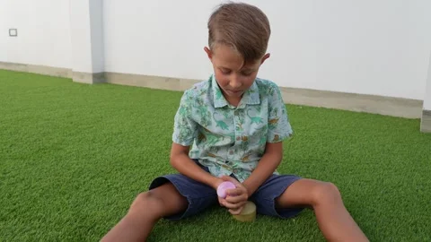 Boy Sitting on Artificial Grass Playing With a Pink Toy Stock Footage 346326541