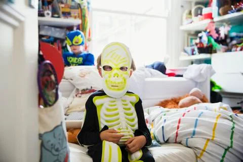 Boy sitting on bed in his room dressed in skeleton costume Stock Photos