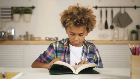 Boy sitting behind table and reading book Video stock 103952276