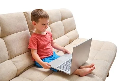 Boy sitting on beige sofa looking at laptop screen. Child using computer for  Fotos Stock