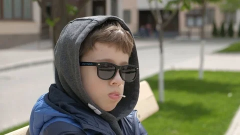 Boy sitting on a bench and eats Lollipop. Rejoices licks the candy, fools around Stock Footage 130117915