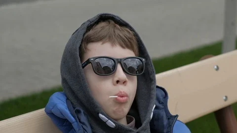 Boy sitting on a bench and eats Lollipop. Rejoices licks the candy, fools around Stock Footage 130117957