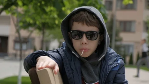 Boy sitting on a bench and eats Lollipop. Rejoices licks the candy, fools around Stock Footage 130117967
