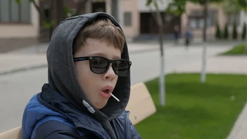 Boy sitting on a bench and eats Lollipop. Rejoices licks the candy, fools around Stock Footage 130117970