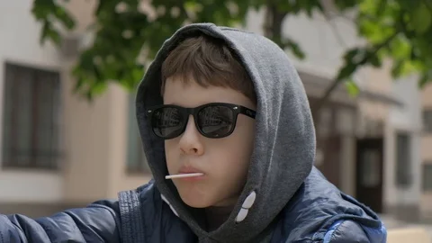 Boy sitting on a bench and eats Lollipop. Rejoices licks the candy, fools around Stock Footage 130117979