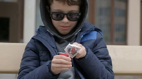 Boy sitting on a bench and ope Lollipop. Rejoices licks the candy, fools around Stock Footage 130117997