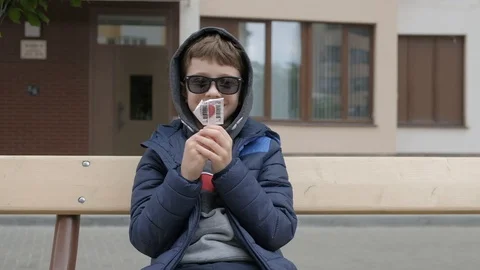 Boy sitting on a bench and open Lollipop. Rejoices licks the candy, fools around Stock Footage 130117996