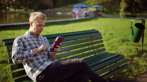 Boy sitting on the bench in the park and browsing internet on tablet Stock Footage 56150992