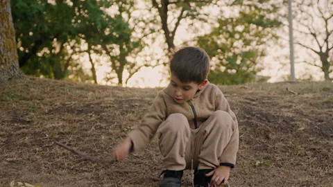 Boy sitting bent over with a stick playing, making dust. Activity for children Video stock 256065947