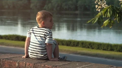 Boy sitting on the brick wall and looking right at the river Stock Footage 79927012