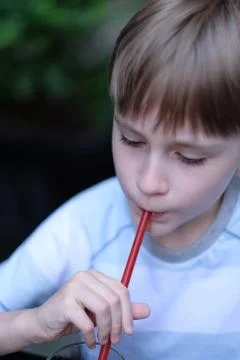 A boy sitting at a cafe table drinks juice through a straw Stock Photos