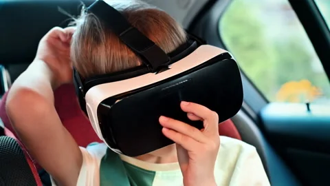 Boy sitting in the car and putting on VR glasses in child safety seat. Slow Stock Footage 250359264
