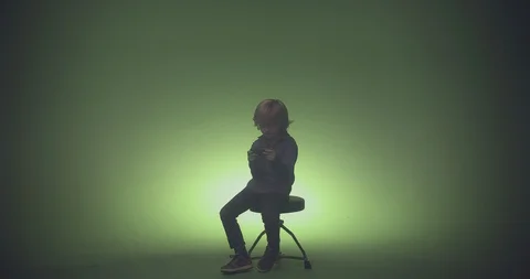 Boy sitting on chair and using mobile phone against green background Stock Footage 99989529