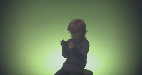 Boy sitting on chair and using mobile phone against green background Stock Footage 99989754