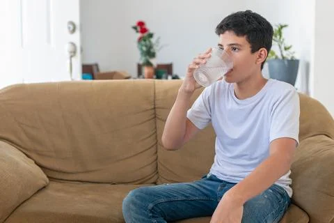 A boy is sitting on a couch and drinking water Stock Photos