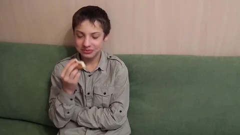 Boy is sitting on the couch and eating bread 库存影片 84478232