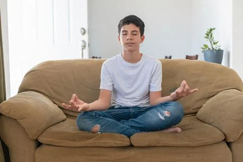 A boy is sitting on a couch and practicing yoga Stock Photos
