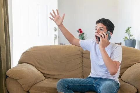 A boy is sitting on a couch and talking on a cell phone Stock Photos