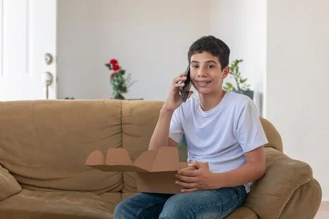A boy is sitting on a couch and talking on a cell phone Stock Photos