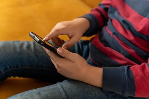 Boy is sitting on the couch and using a smartphone Stock Photos