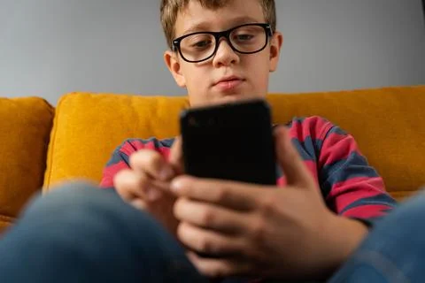 Boy is sitting on the couch and using a smartphone Stock-Fotos