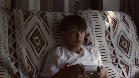 A boy sitting on a couch iplaying video games Stock Footage 244771679
