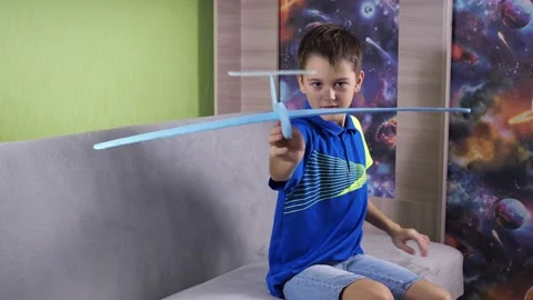 The boy is sitting on the couch playing with a blue airplane. the plane is made Stock Footage 164234380