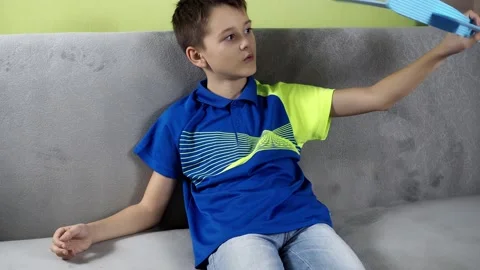 The boy is sitting on the couch playing with a blue airplane. the plane is made Stock Footage 166738095