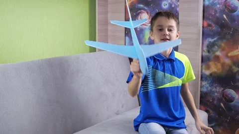 The boy is sitting on the couch playing with a blue airplane. the plane is made Stock Footage 167904924