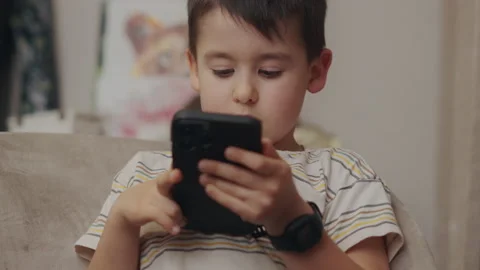 Boy sitting on couch using smartphone and playing video games on internet online Stock Footage 239726092