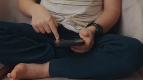 Boy sitting on cozy sofa at home holding phone, playing games. Caucasian healthy Stock Footage 240730187