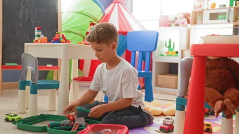 Boy sitting crosslegged assembling toy tools and small cars with bare hands.. Stock Footage 337373171