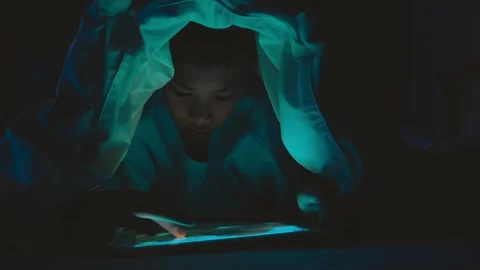 A boy is sitting in a dark room with a tablet in his hand Stock Footage 318863438