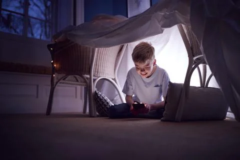 Boy Sitting In Den Or Camp He Has Made At Home Playing With Mobile Phone Stock Photos
