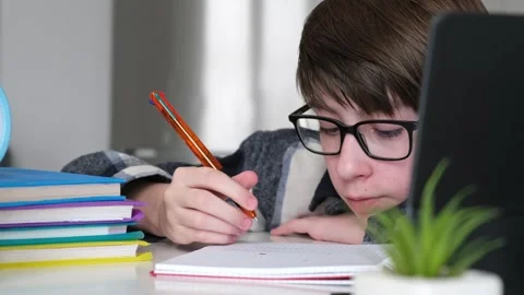 A boy is sitting at a desk with a stack of books and a laptop Stock Footage 321479813