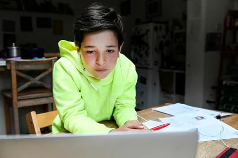 A boy sitting at a desk using a laptop for an interactive learning session, home Stock Photos
