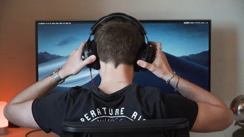 Boy sitting down at computer, putting on headphones, editing videos, 4K Stock Footage 129616181