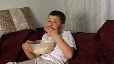 Boy sitting eating popcorn and watching movie at home Stock Footage 154406152