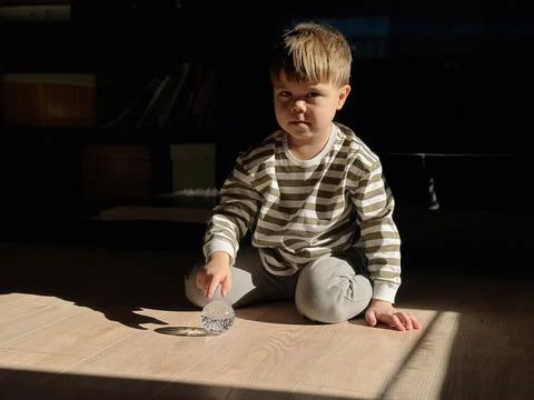 Boy sitting on the floor and exploring a glass sphere in warm sunlight at h.. 스톡 사진