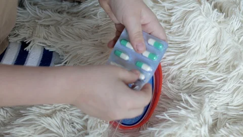 The boy is sitting on the floor on a blanket, squeezing pills out of the package Stock Footage 128072630