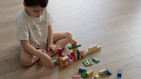 Boy sitting on the floor building constructor tower from colorful wooden blocks Stock Footage 170035593